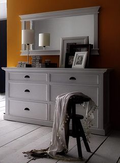 a white dresser sitting in front of a mirror on top of a wooden floor next to a lamp