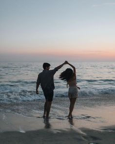 two people standing on the beach holding hands