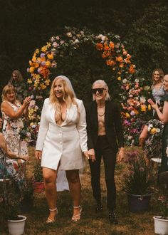 two women are walking down the aisle at a wedding with flowers all around them and one woman is holding her hand