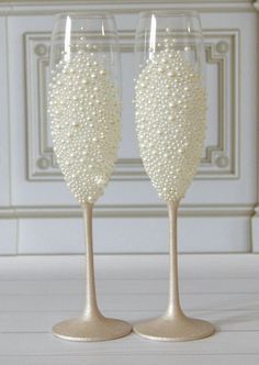 two wine glasses with pearls on them sitting next to each other in front of a wall