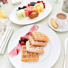 waffles, fruit and coffee on a white tablecloth with utensils