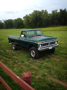 an old pickup truck parked in a grassy field next to a wooden fence on a cloudy day