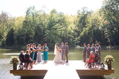 a group of people standing on top of a wooden pier next to a lake with trees in the background