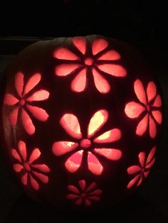 a carved pumpkin decorated with flowers on it's side and lit up in the dark