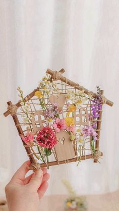 a person holding up a small house made out of sticks with flowers on top of it