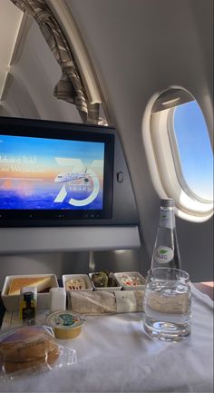 an airplane seat with food on the table and a television screen in the back ground