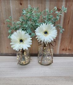 two vases with white flowers are sitting on a wooden table next to each other