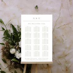 a wedding seating chart sitting on top of a wooden easer next to flowers and greenery