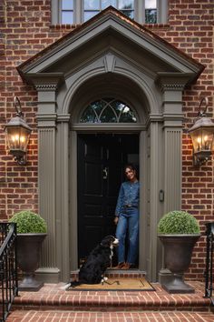 a woman standing in front of a black door with a dog on the steps next to her