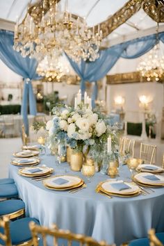 a table with blue and gold plates, silverware and flowers on it is set up for a formal dinner