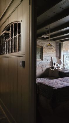 an open door leading to a bedroom with a bed and chair in it, next to a brick wall