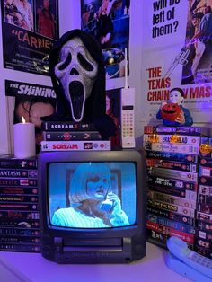 a television with a scary mask on top of it next to a pile of dvd's