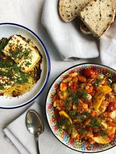 two plates of food on a table with bread and spoons next to it,