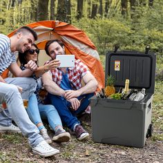 three people are sitting in front of a tent and taking a selfie with their cell phone