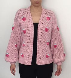 a woman standing in front of a white wall wearing a pink knitted cardigan