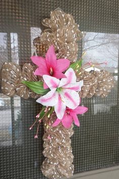 a cross decorated with pink flowers in front of a window