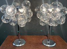 two clear glass flower shaped lamps on metal bases with lights shining in the back ground