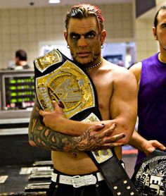 two men standing next to each other with their arms around one another and holding wrestling belts