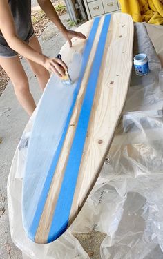 a woman sanding next to a surfboard on top of a plastic wrapper