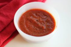 a white bowl filled with red sauce on top of a table next to a red towel