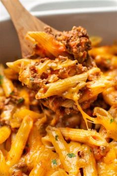 a wooden spoon full of pasta with meat and parmesan cheese on it in a white bowl