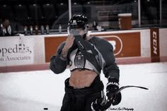 a hockey player is standing on the ice and holding his helmet up to his face