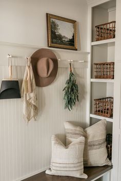 a bench with pillows and hats on it in front of a wall mounted coat rack