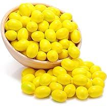 a wooden bowl filled with yellow candies on top of a white table next to it