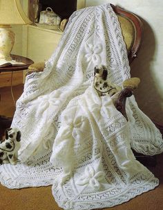 a white crocheted blanket sitting on top of a chair next to a cat