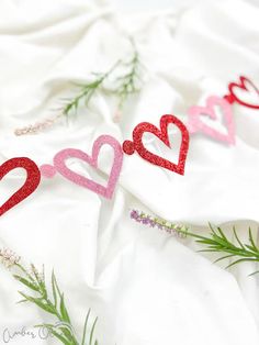 two hearts cut out of paper sitting on top of a white sheet with greenery