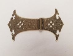 an antique brass buckle with decorative designs on the front and sides, set against a plain white background