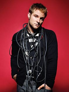 a man standing in front of a red wall with headphones around his neck and hands on his hips