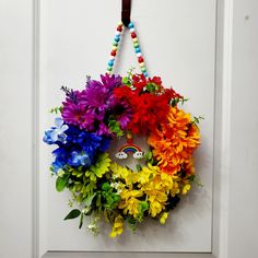 a wreath with flowers and beads hanging on the front door, decorated with rainbow colors