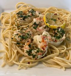 a plate of pasta with shrimp and lemon wedges