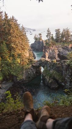 a person laying on the ground with their feet up looking out at water and trees