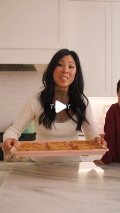 two women sitting at a kitchen counter with food on a plate in front of them