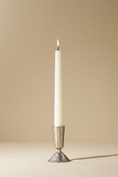 a single white candle sitting on top of a metal stand with a long shadow coming from it