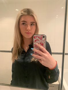 a woman taking a selfie in front of a bathroom mirror with her cell phone