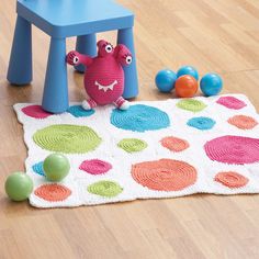 a crocheted rug on the floor with balls and a chair in the background