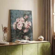 a painting sitting on top of a green cabinet next to a vase filled with flowers