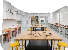 a room filled with lots of wooden tables and yellow stools next to each other