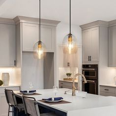 a kitchen with two pendant lights hanging from the ceiling and an island in front of it