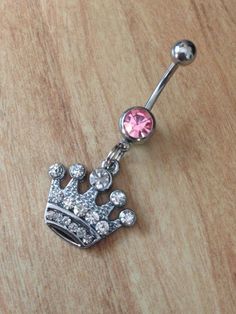 a pink jeweled crown belly ring on a wooden table