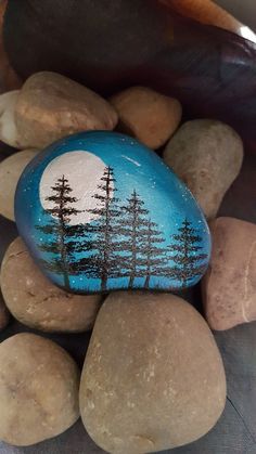 a painted rock sitting on top of some rocks with trees in the middle and moon behind it