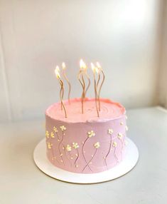 a pink cake with white flowers on it and lit candles sticking out of the top