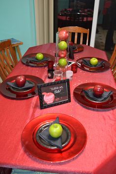 the table is set with red plates and place settings for an apple themed dinner party