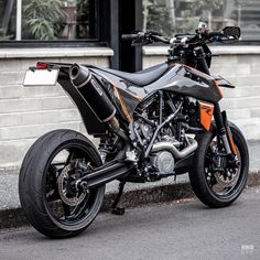 an orange and black motorcycle parked on the side of the road next to a building