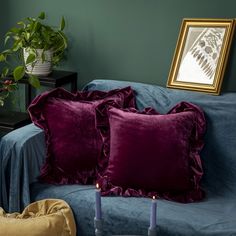 two purple pillows on a blue couch in front of a painting and potted plant