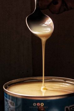 a person pouring sauce on top of a can of food with a spoon in it