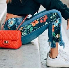 a woman is sitting on the curb with her hand in her pocket and holding a red purse